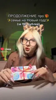 Кадр из видео: девушка сидит за столом и держит красиво упакованный подарок, в ролике показывает коробку и говорит о сумме для семьи.