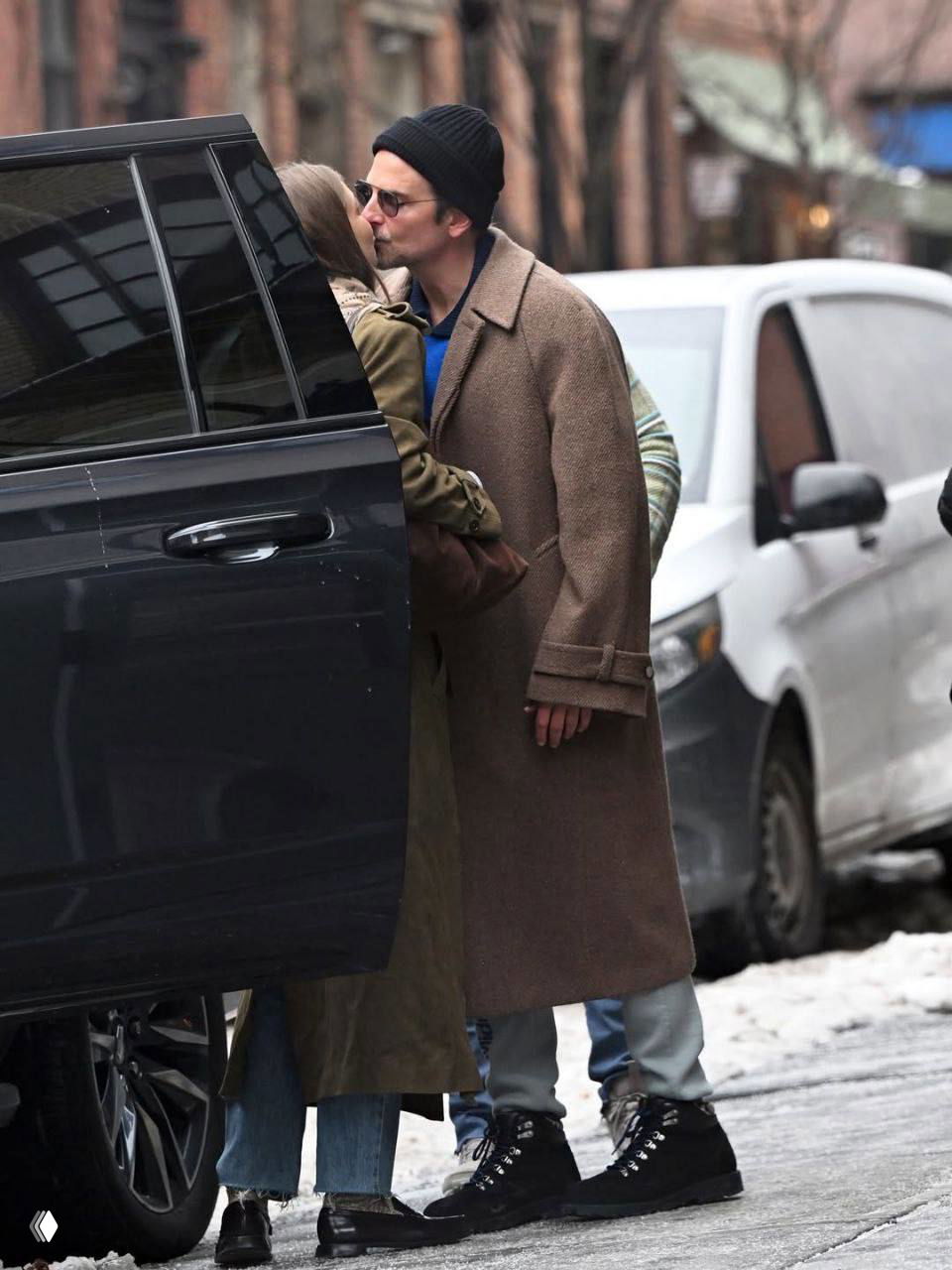 Момент у машины: пара обнимается перед посадкой, видны припаркованные автомобили и заснеженная улица — уличная папарацци-сцена.