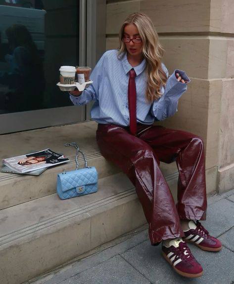 Девушка с кофейными стаканами в руках в небесно-голубой рубашке и бордовыми кожаными брюками, уличная сцена рядом с кафе.