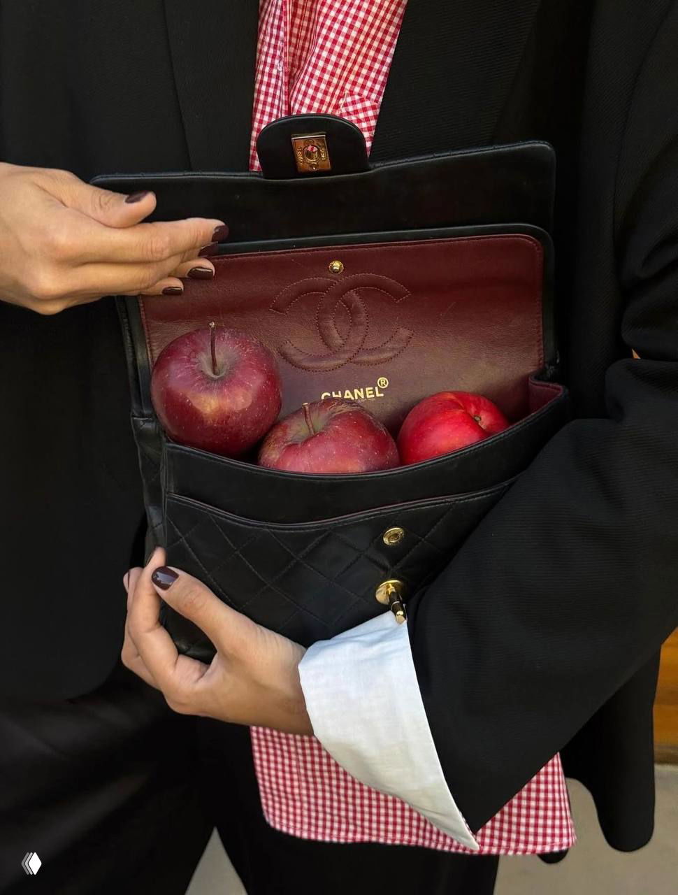 Открытая сумка с логотипом и несколькими красными яблоками внутри; художественная сцена с аксессуаром и насыщенным красным оттенком.