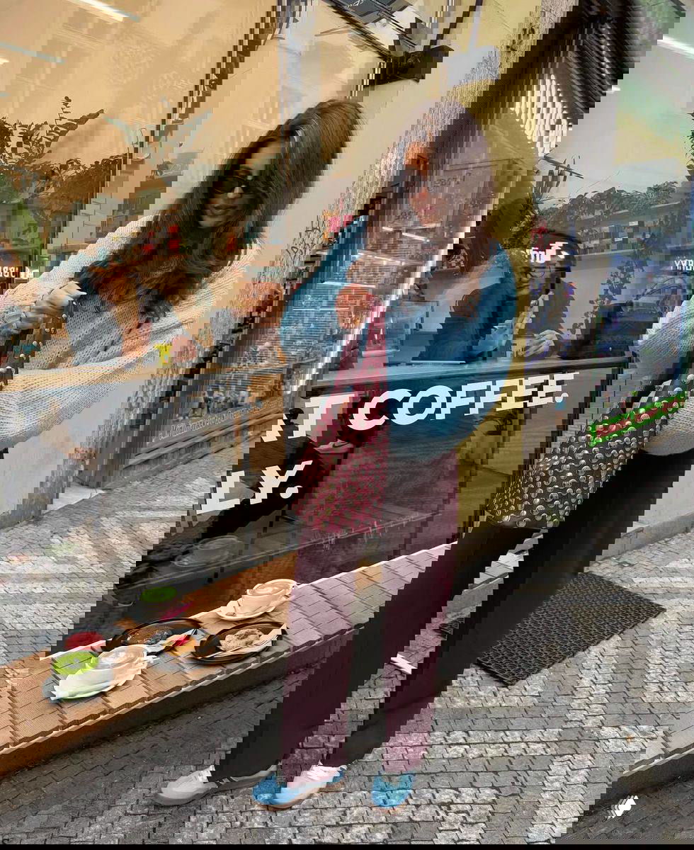 Полноразмерный уличный образ: светло-голубой объемный свитер и бордовые прямые брюки, голубые туфли и бордовая сумка с заклепками.