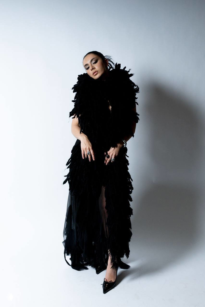 Charli XCX в полный рост в текстурном чёрном наряде с аксессуарами — кадр из фотосессии/клипа, образ разработан Daniil Antsiferov.
