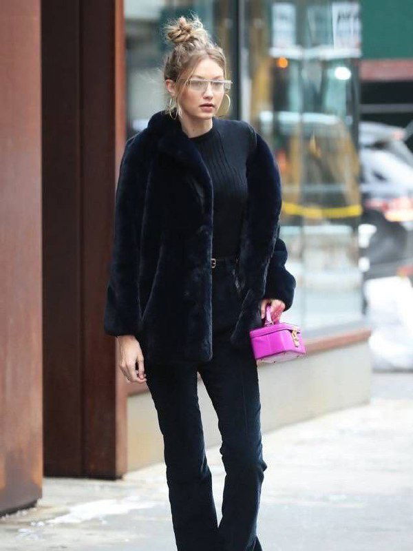 Уличный портрет: женщина в тёмной шубе и чёрных брюках держит небольшую розовую сумочку, идёт по городскому тротуару.