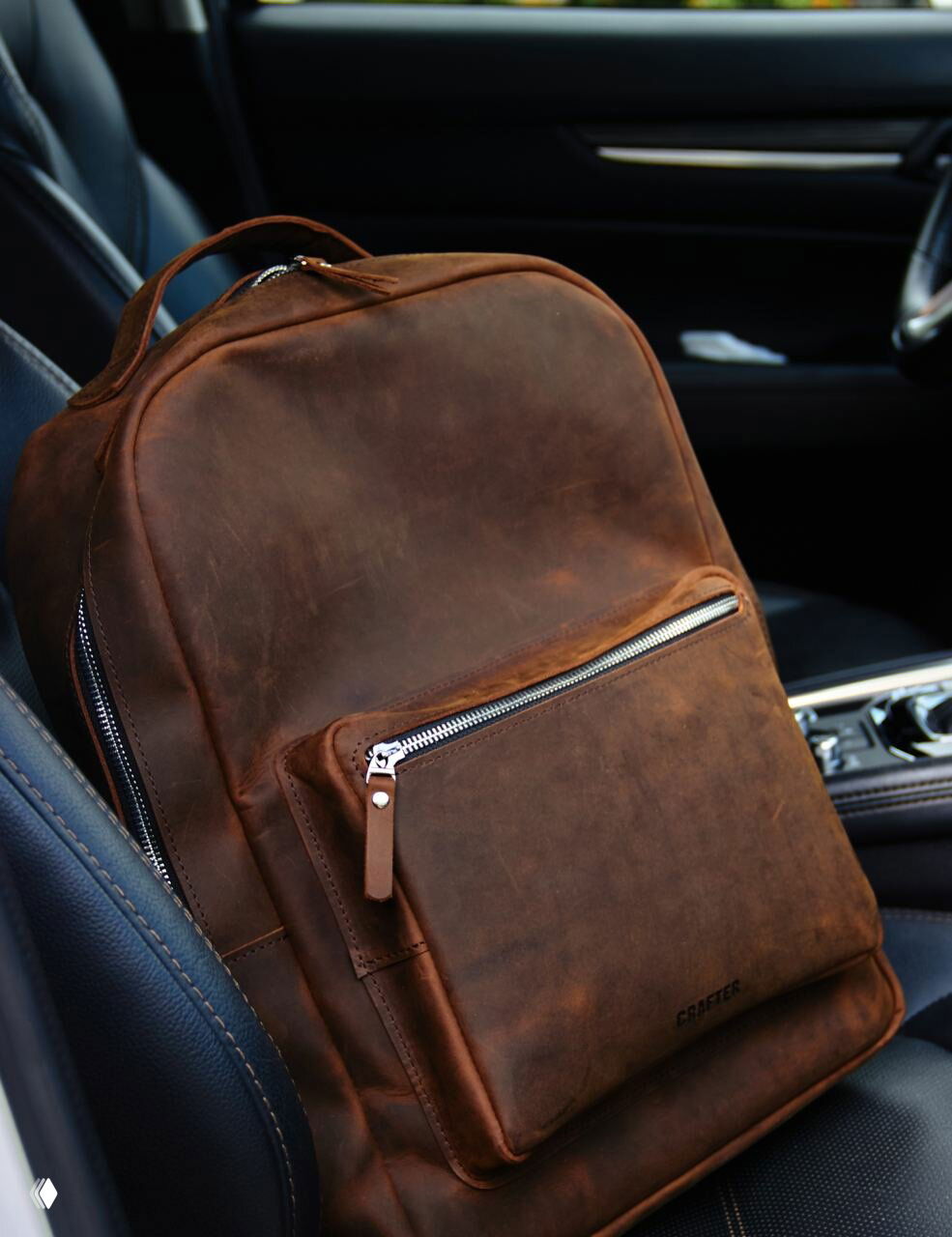 Коричневый кожаный рюкзак с наружным карманом и металлической молнией, крупный план на переднюю часть и текстуру кожи.