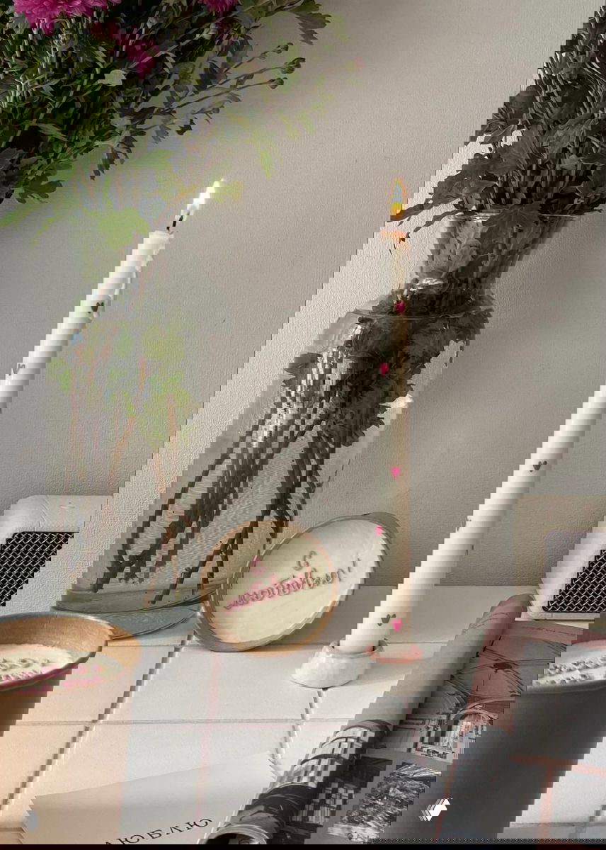 Фото одной зажжённой тонкой свечи с небольшими сердечками рядом с вазой с цветами и керамической тарелкой с надписью «С любовью»