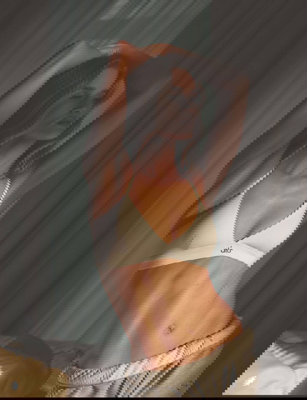 Портретная фотография модели в белом бра и серых штанах, мягкий боковой свет подчёркивает силуэт и текстуру кожи, акцент на позе.