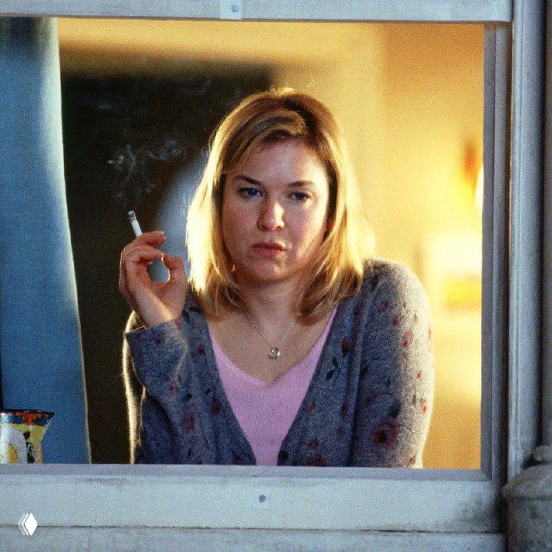Женщина у окна с сигаретой в руках, задумчивое выражение лица — кадр из ироничной экранизации о личной жизни и самооценке.
