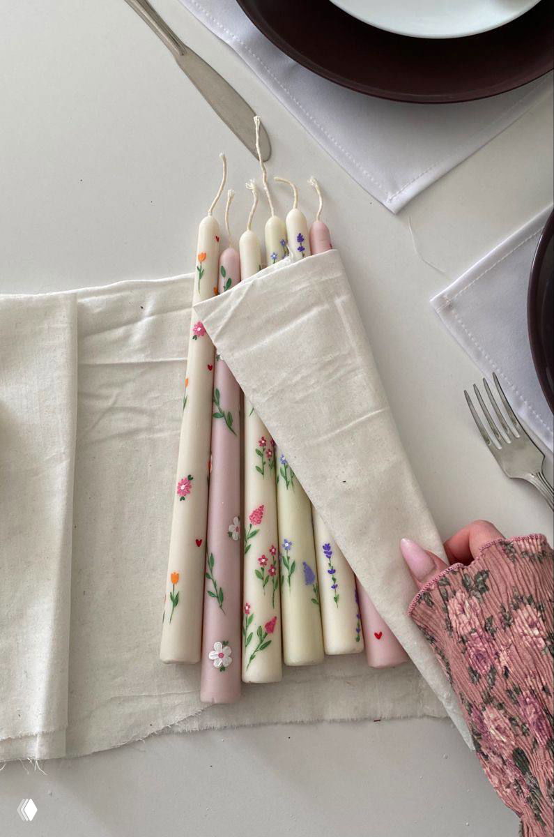 Фото набора тонких свечей с ручной росписью цветочных мотивов, завернутых в тканевый футляр; видна рука с розовым маникюром