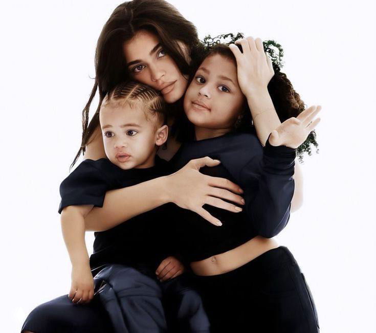 Женщина обнимает двух маленьких детей в семейной студийной фотосессии на светлом фоне — тёплый семейный портрет без указания имён.