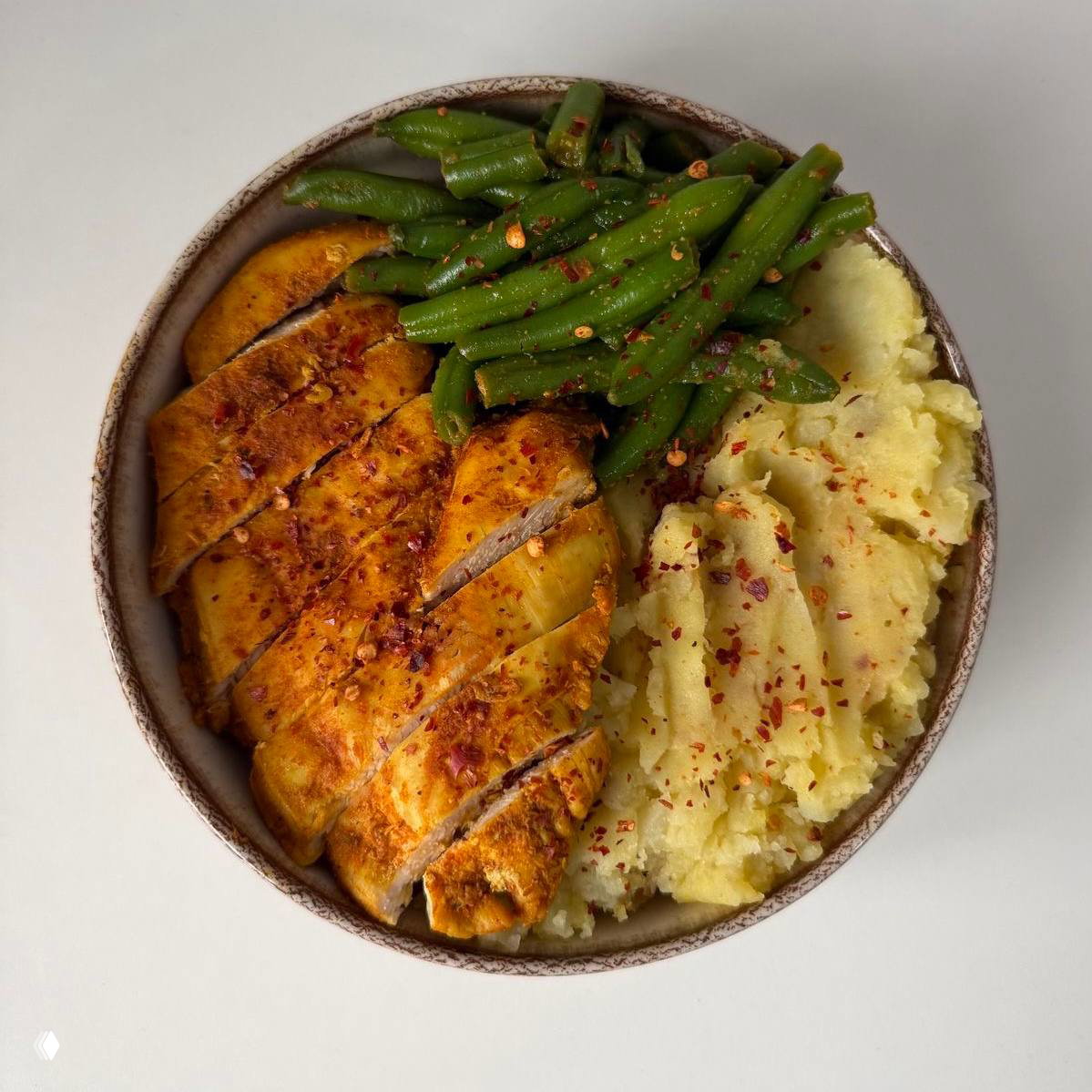 Миска с нарезанной пряной куриной грудкой, стручковой зелёной фасолью и картофельным пюре, приправленным хлопьями чили — будничное блюдо.