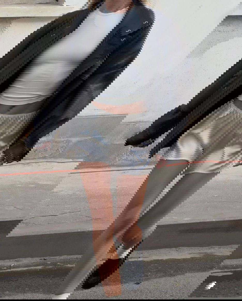 Крупный кадр: атласные серебристые шорты с кружевом в сочетании с укороченным белым топом и массивной кожаной курткой — минималистичный стритстайл.