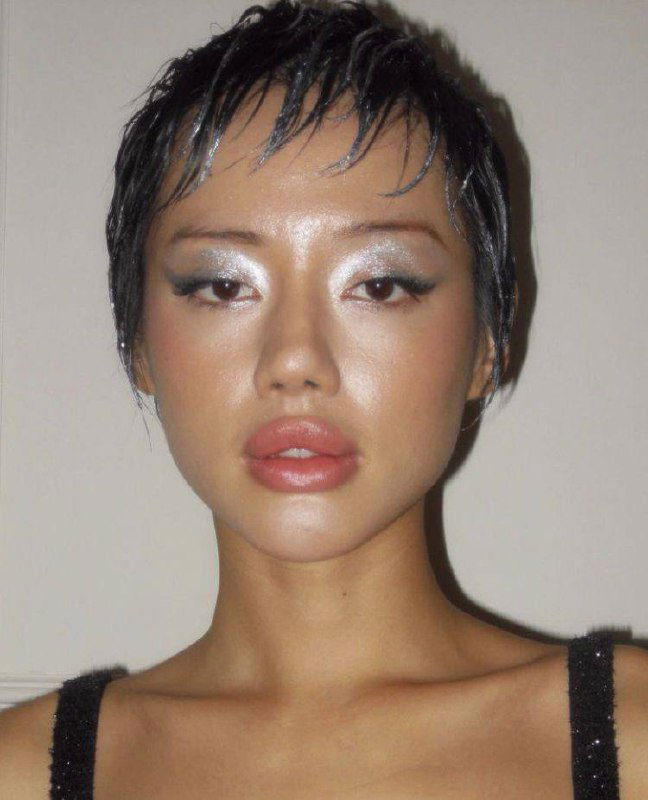 Портрет модели с ярким серебристым макияжем глаз и нейтральными губами; прическа короткая, взгляд в камеру, акцент на текстуре кожи и тенях.