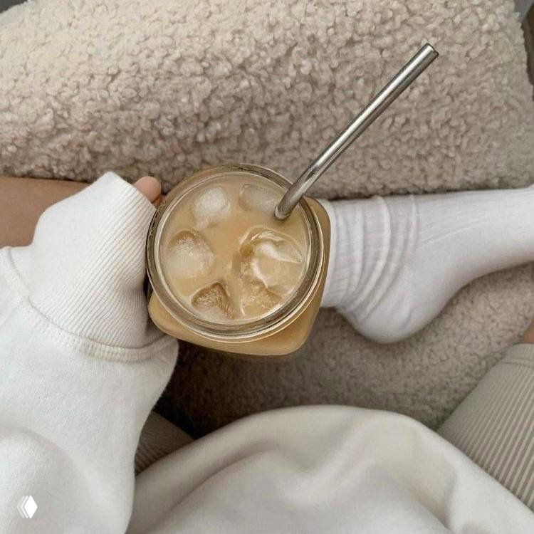 Низкий ракурс на руки с холодным кофе в банке со льдом, белые носки и уютный текстиль — момент кофе-брейка в пастельной палитре.