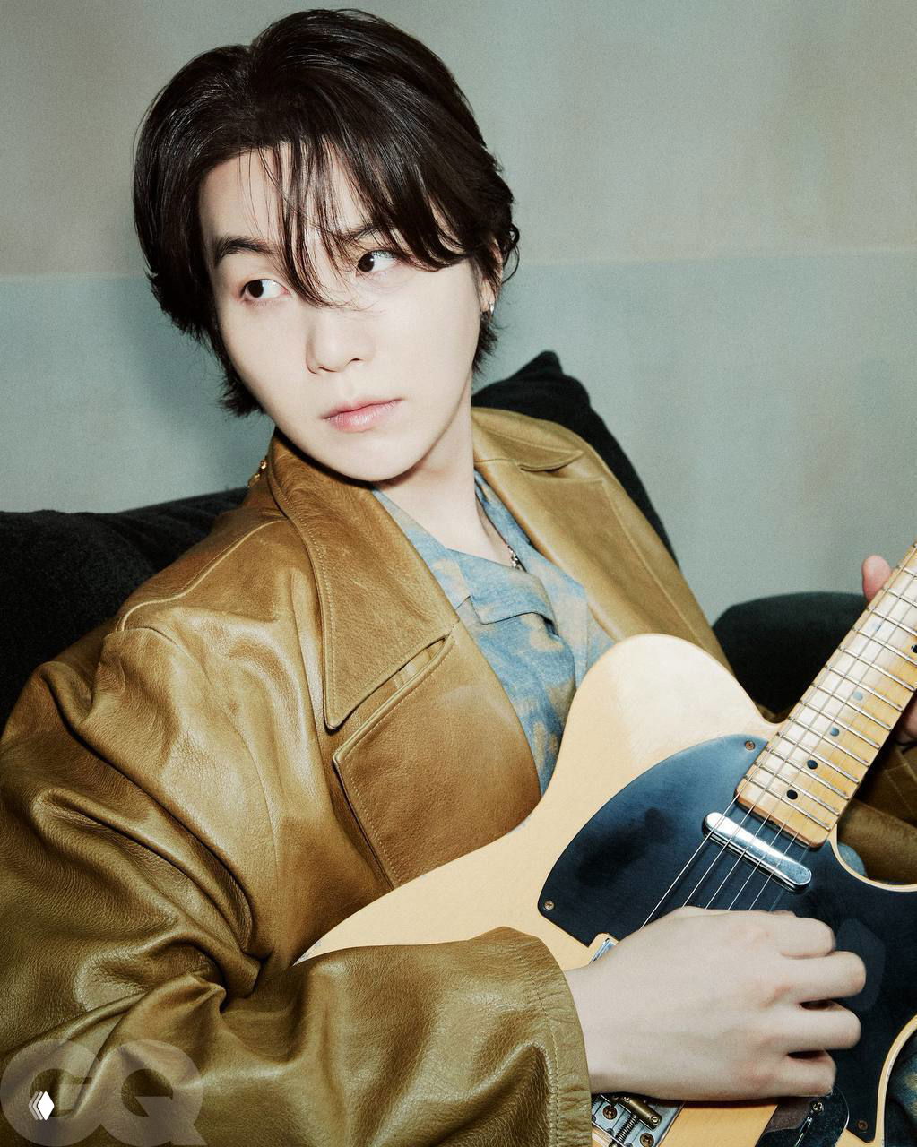 Портретный снимок участника BTS с гитарой: мягкое освещение, кожаная куртка и задумчивый взгляд в кадре для GQ.