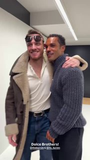 Фото: на фоне студии моды два мужчины обнимаются после показа — слева в дублёнке и солнцезащитных очках, справа в тёмной водолазке.