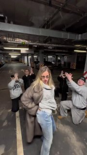 Четверо в повседневной одежде в подземной парковке; кадр с поднятыми руками и живой, танцевальной атмосферой в клиповом стиле.