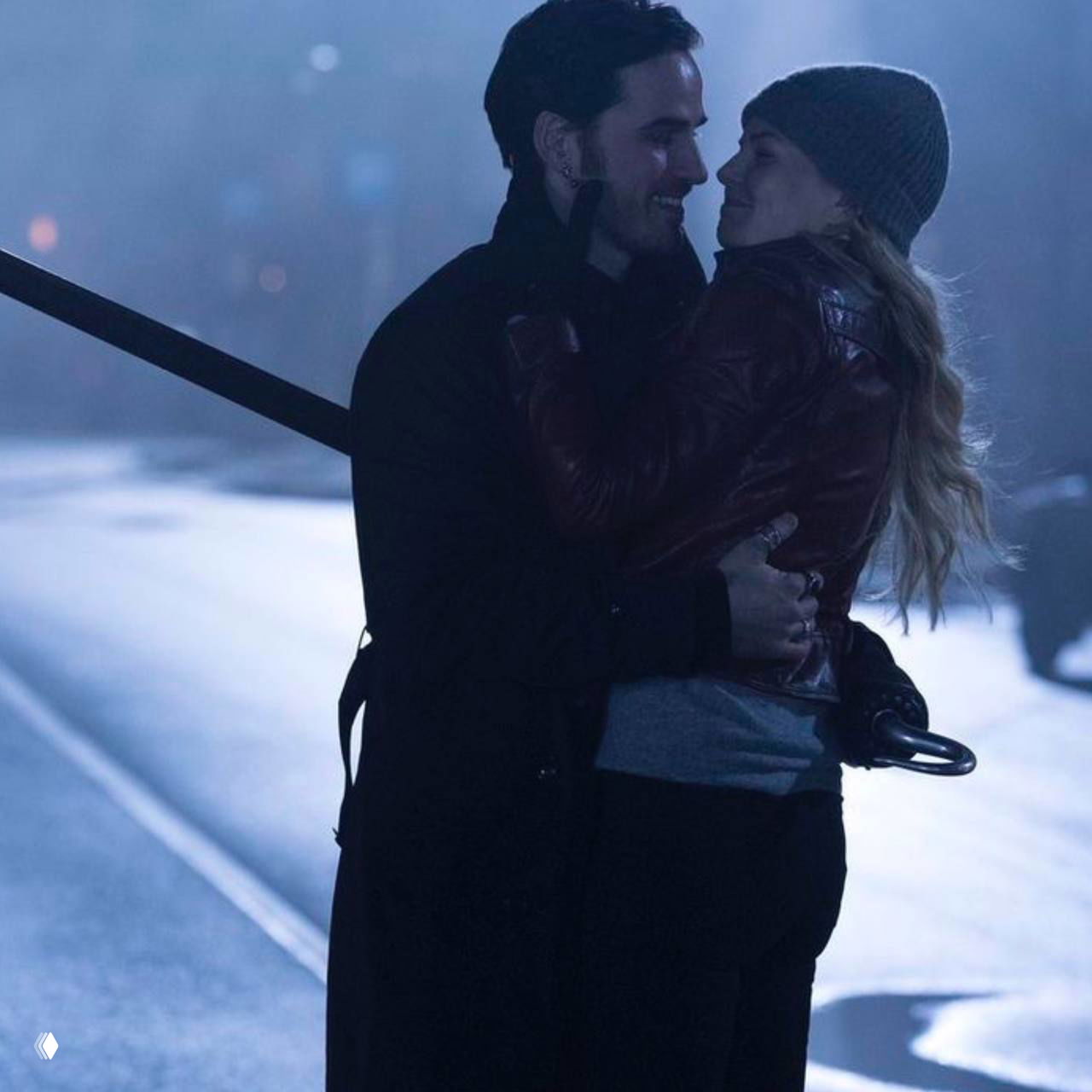 Эмма и Киллиан ночью на улице: он держит её в руках, городской фон и холодный свет улицы создают атмосферу защиты и уюта.