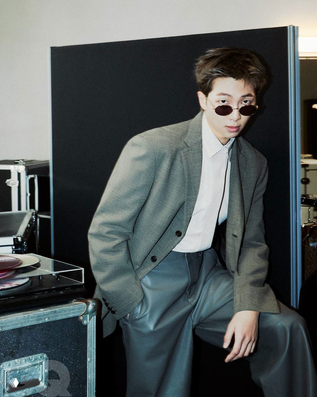 Портрет участника BTS в сером пиджаке и солнечных очках на фоне реквизита; атмосферный кадр из GQ-фотосессии.