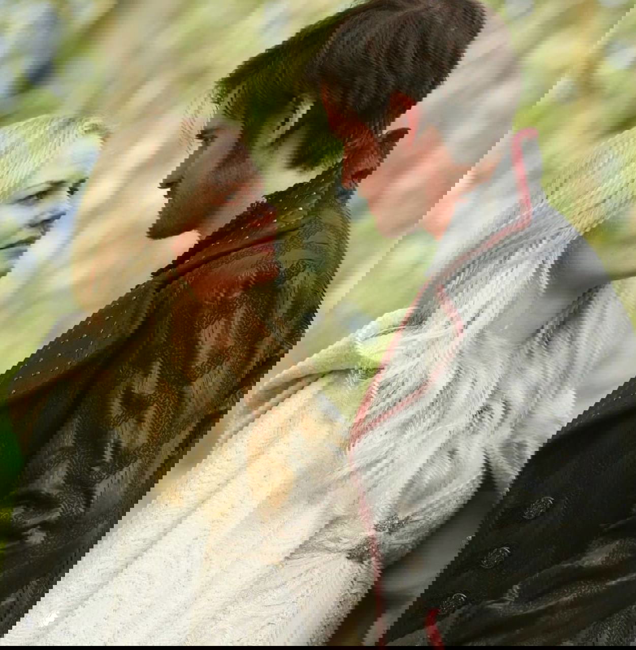 Портретный кадр в лесном антураже: Эмма в светлом плаще и Киллиан в тёмном пальто стоят лицом друг к другу, атмосфера сказочности.