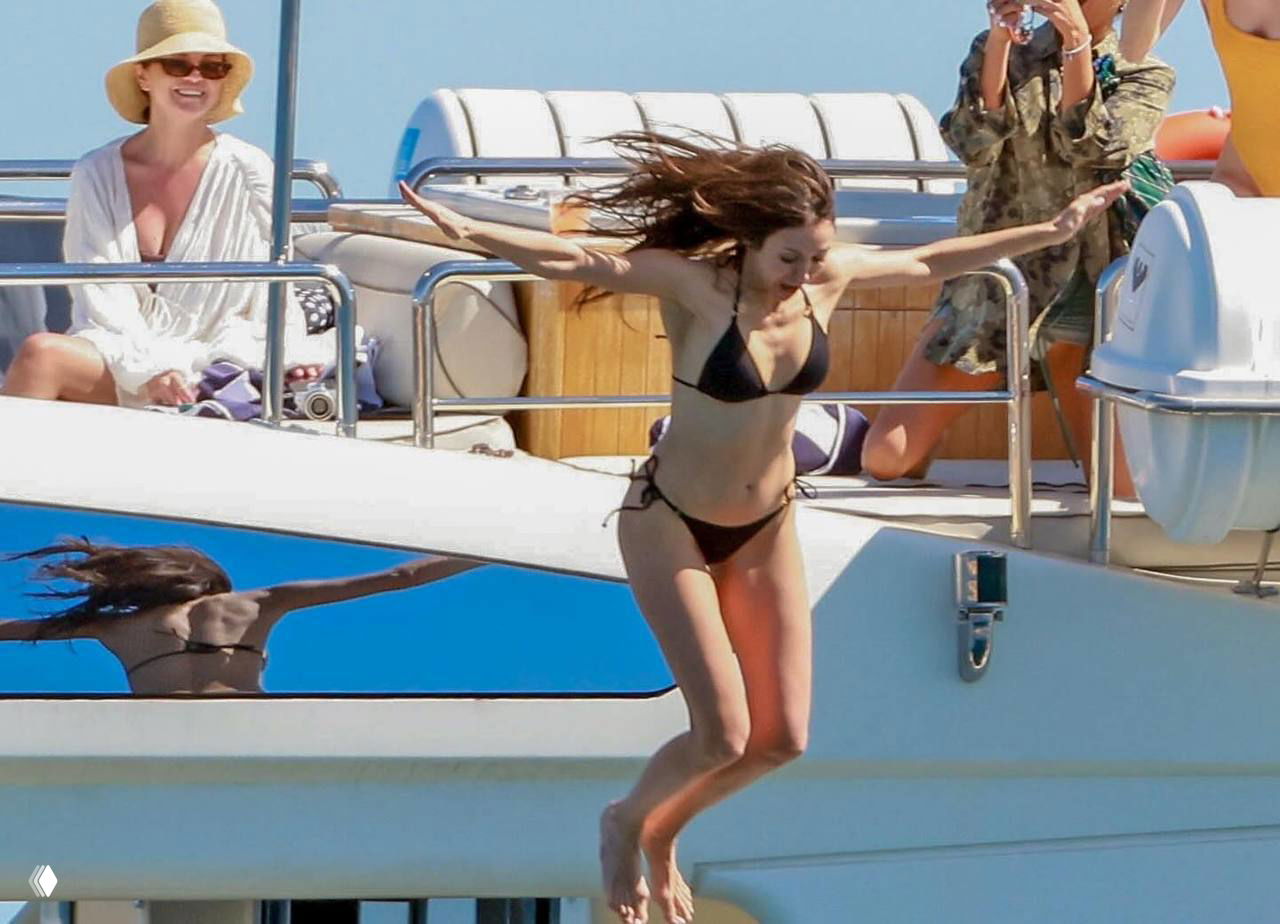 Селена Гомес прыгает с борта яхты в воду в черном бикини, за ней видна палуба и отражение — динамичный кадр отдыха на море.
