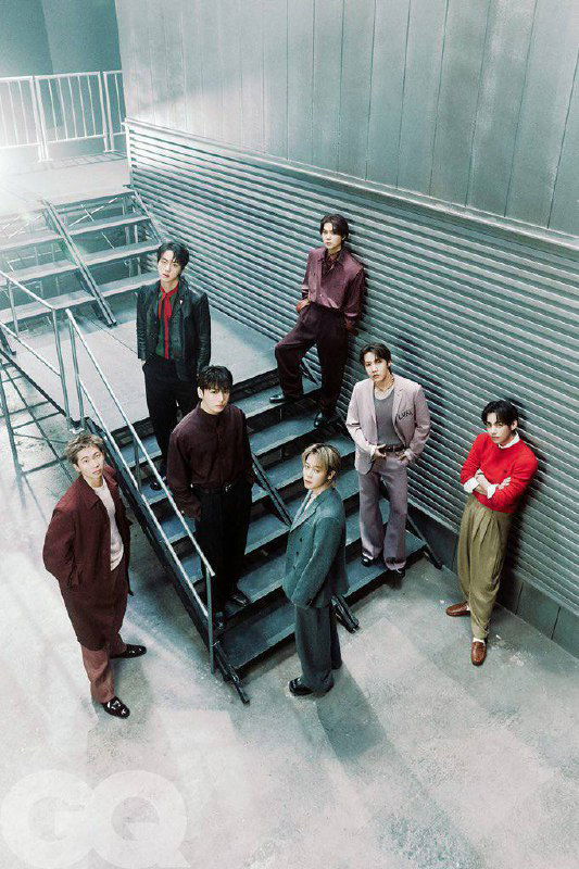 Групповой снимок BTS на лестнице в модных костюмах — полный состав в кадре, стилизованный интерьер и фирменный логотип GQ.
