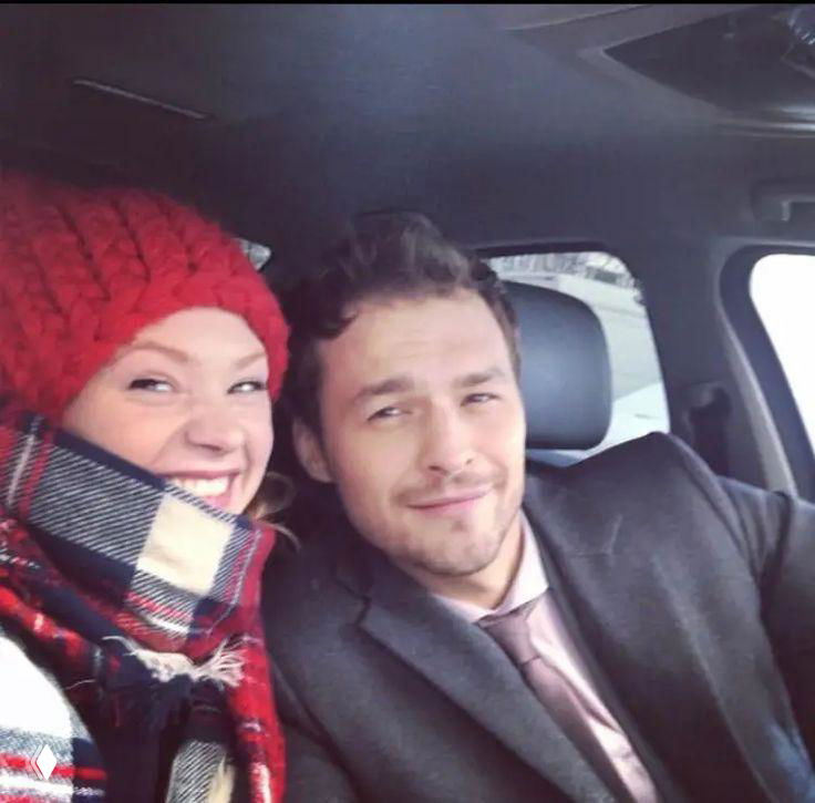 Неофициальное селфи в автомобиле: женщина в яркой вязаной шапке и мужчина улыбаются в камеру, закадровая, живая эмоция.