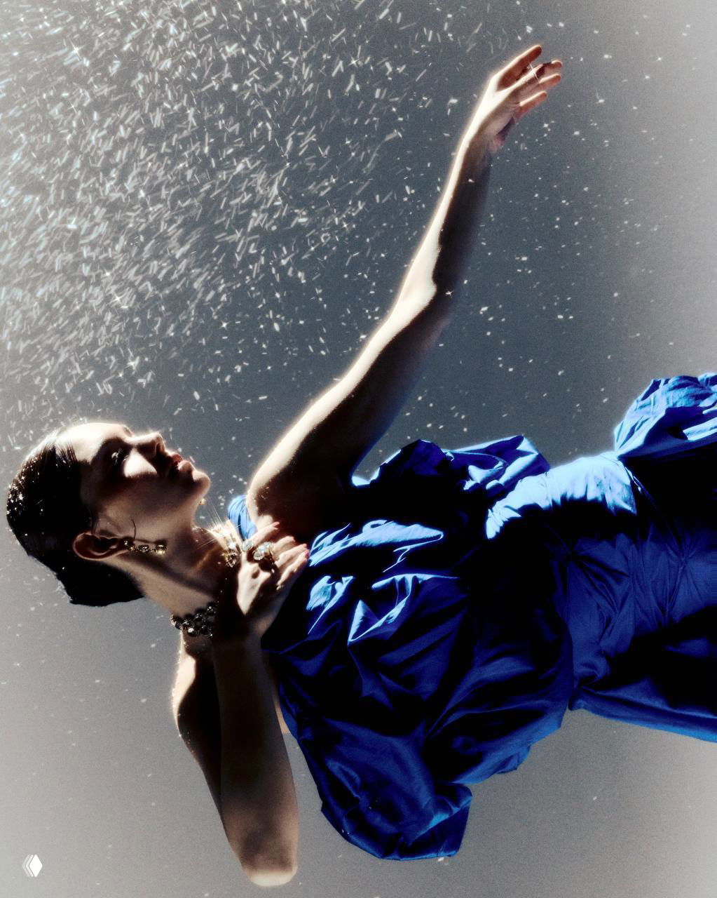 Драматичный кадр с поднятой рукой и размытым световым эффектом, женщина в синем платье в танцевальной позе под кинематографичный свет.