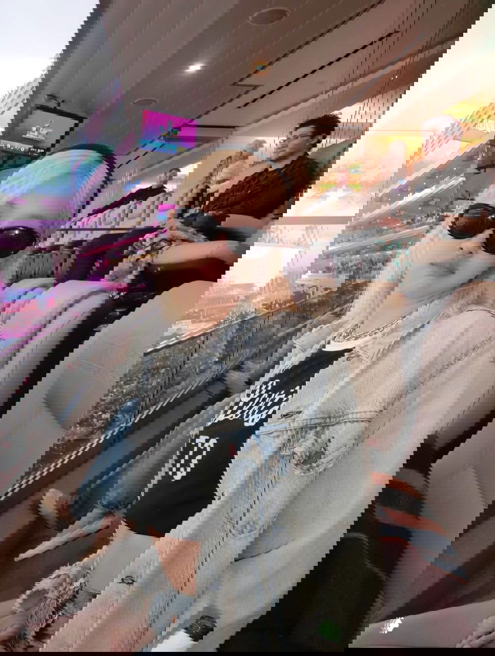 Портрет женщины в солнцезащитных очках и джинсовой куртке в ложах стадиона; на заднем плане зрительские секторы и экраны матча.