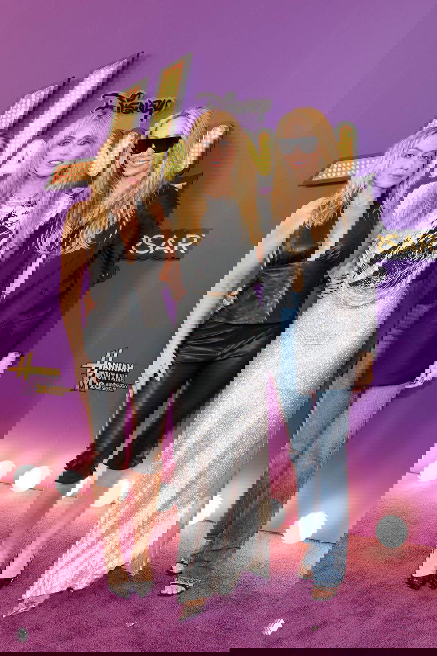 Группа гостей, включая Майли Сайрус, позирует перед фиолетовым пресс‑воллом с надписью «Hannah Montana 20th Anniversary», фото с красной дорожки события.