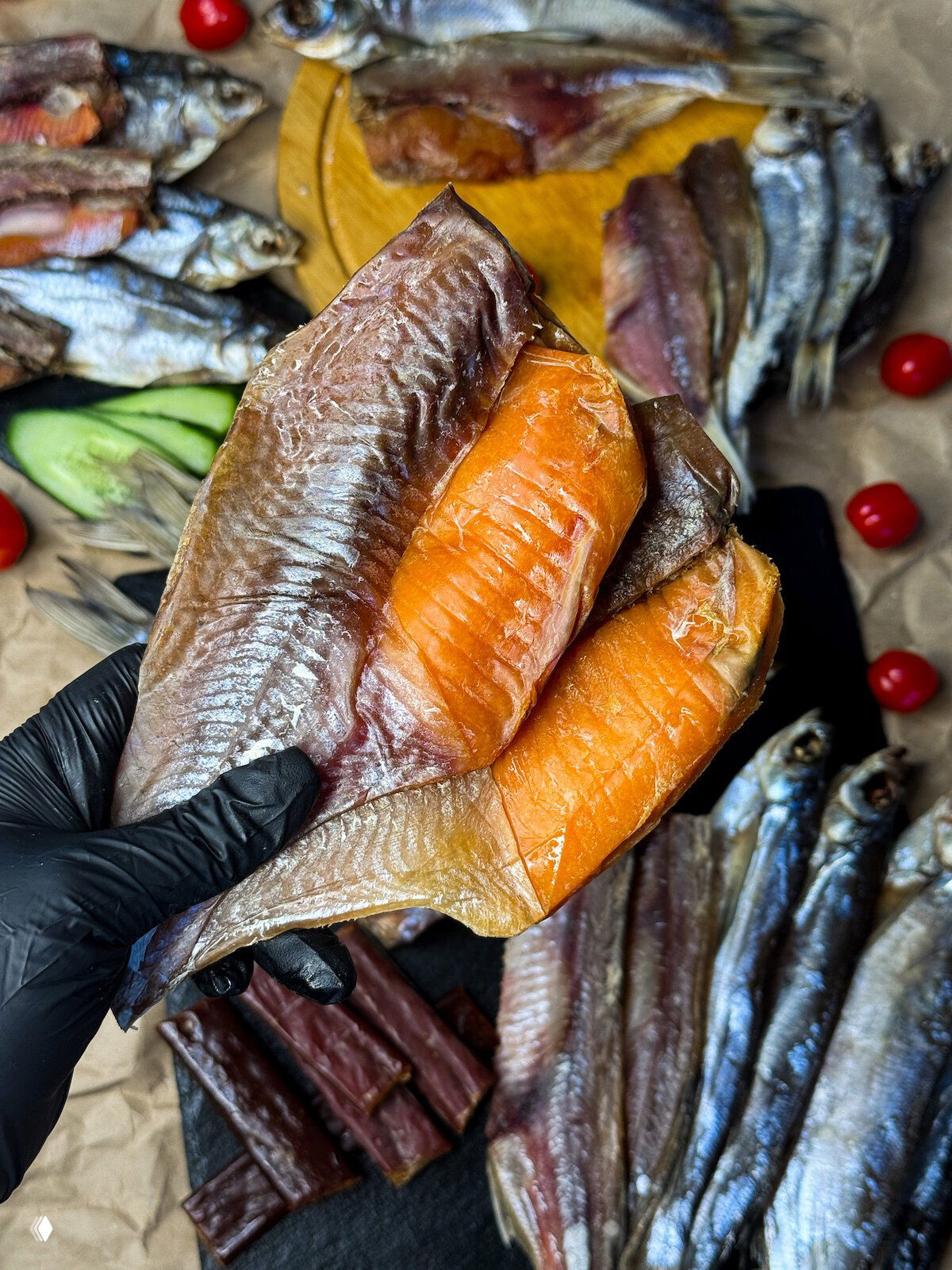Рука в чёрной перчатке держит крупные филе вяленой рыбы с яркой оранжевой мякотью, на фоне прочего ассортимента снеков.