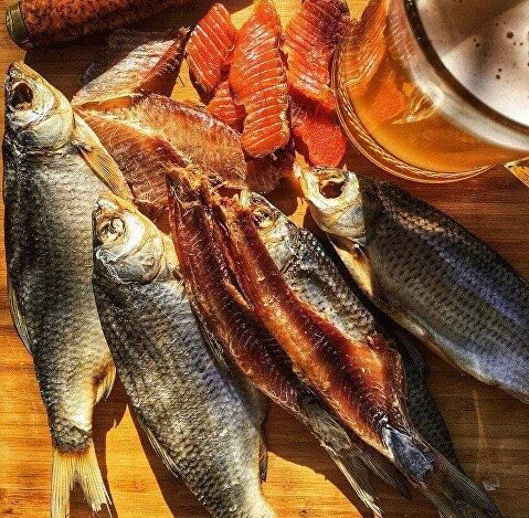 Небольшой кадр с разложенными вялеными рыбками на деревянной доске и светлым фоном, показаны разные формы и размеры снеков.