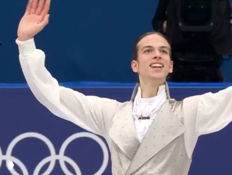 Кадр с улыбающимся Пётром Гуменником на льду; изображение искажено цифровыми шумами и пикселизацией, видна эмблема Олимпиады.