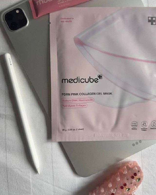 Розовая упаковка маски Medicube PDRN Pink Collagen Gel Mask лежит рядом с планшетом, Apple Pencil и декоративной заколкой — бьюти-flatlay в розовых тонах.