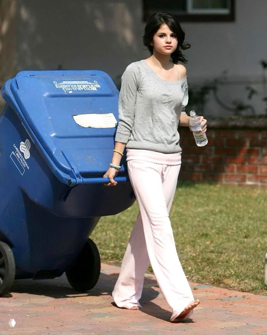 Селена Гомес идёт босиком в розовых штанах и сером свитере рядом с мусорным баком — непринуждённый домашний лук из 2010-х.
