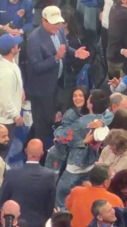 Вид с трибун на болельщиков во время матча NBA: пара рядом с другими зрителями, заметны джинсы с сине‑оранжевыми крестами и оживлённая арена.