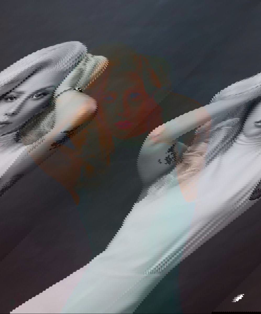 Студийный портрет женщины с платиновыми волосами и татуировками на руках на нейтральном фоне, художественная постановка.