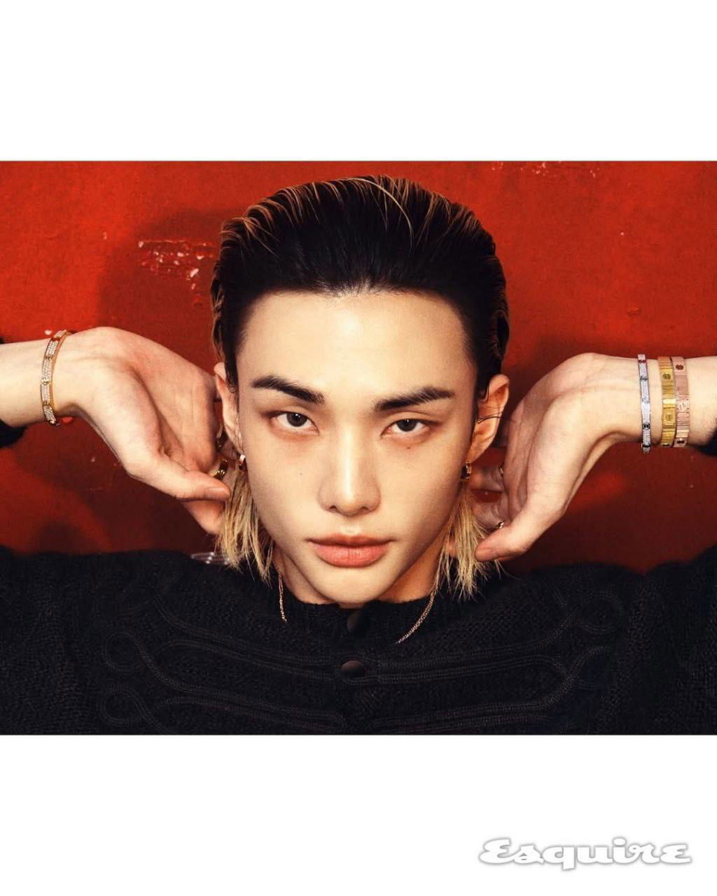 Крупный план лица молодого айдола на красном фоне, минималистичный макияж и прическа, акцент на серьгах и выражении взгляда в студийной съёмке.