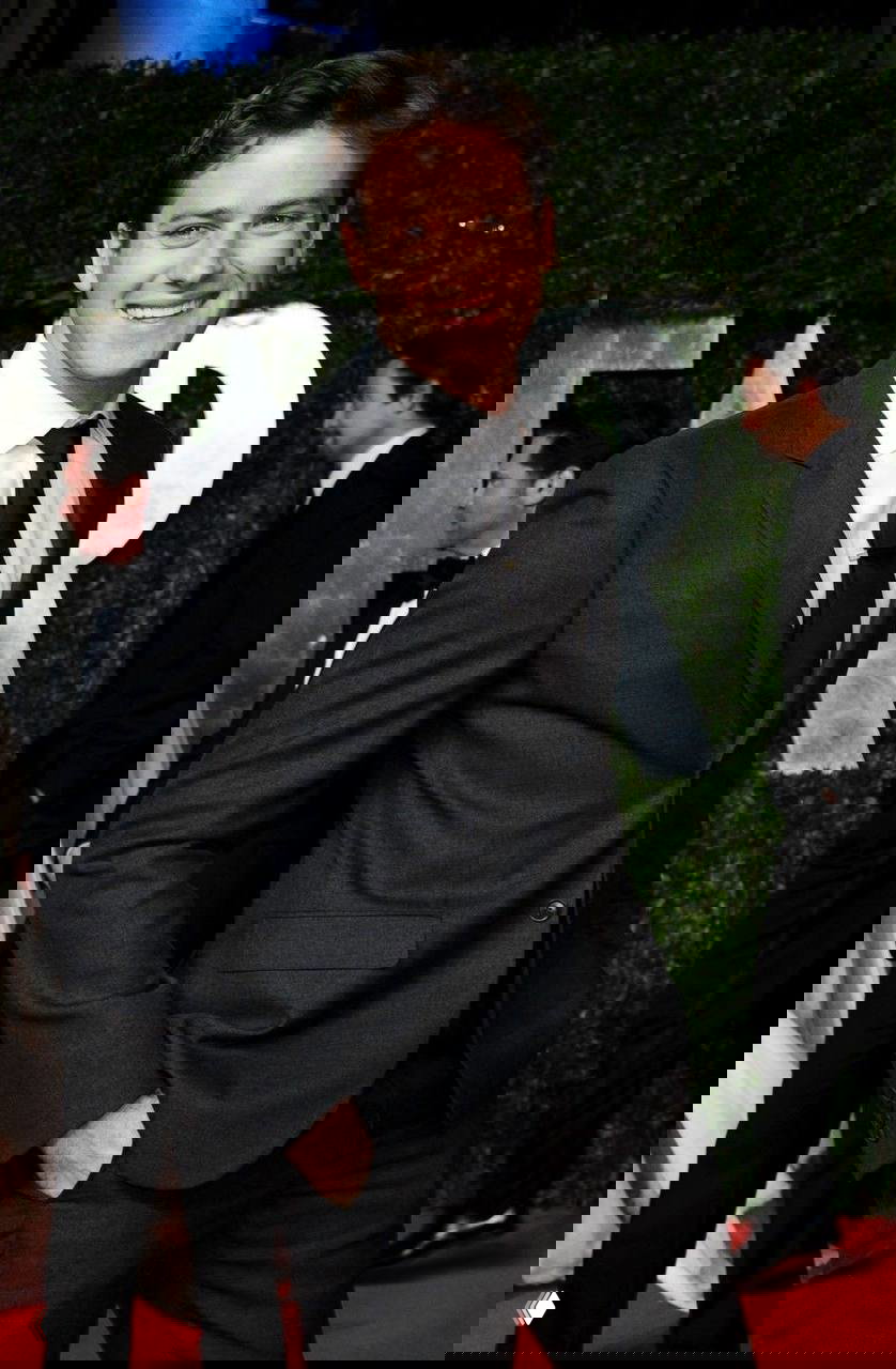 Портрет мужчины в темном костюме на красной дорожке: крупный план улыбающегося человека на светском мероприятии, торжественная атмосфера.