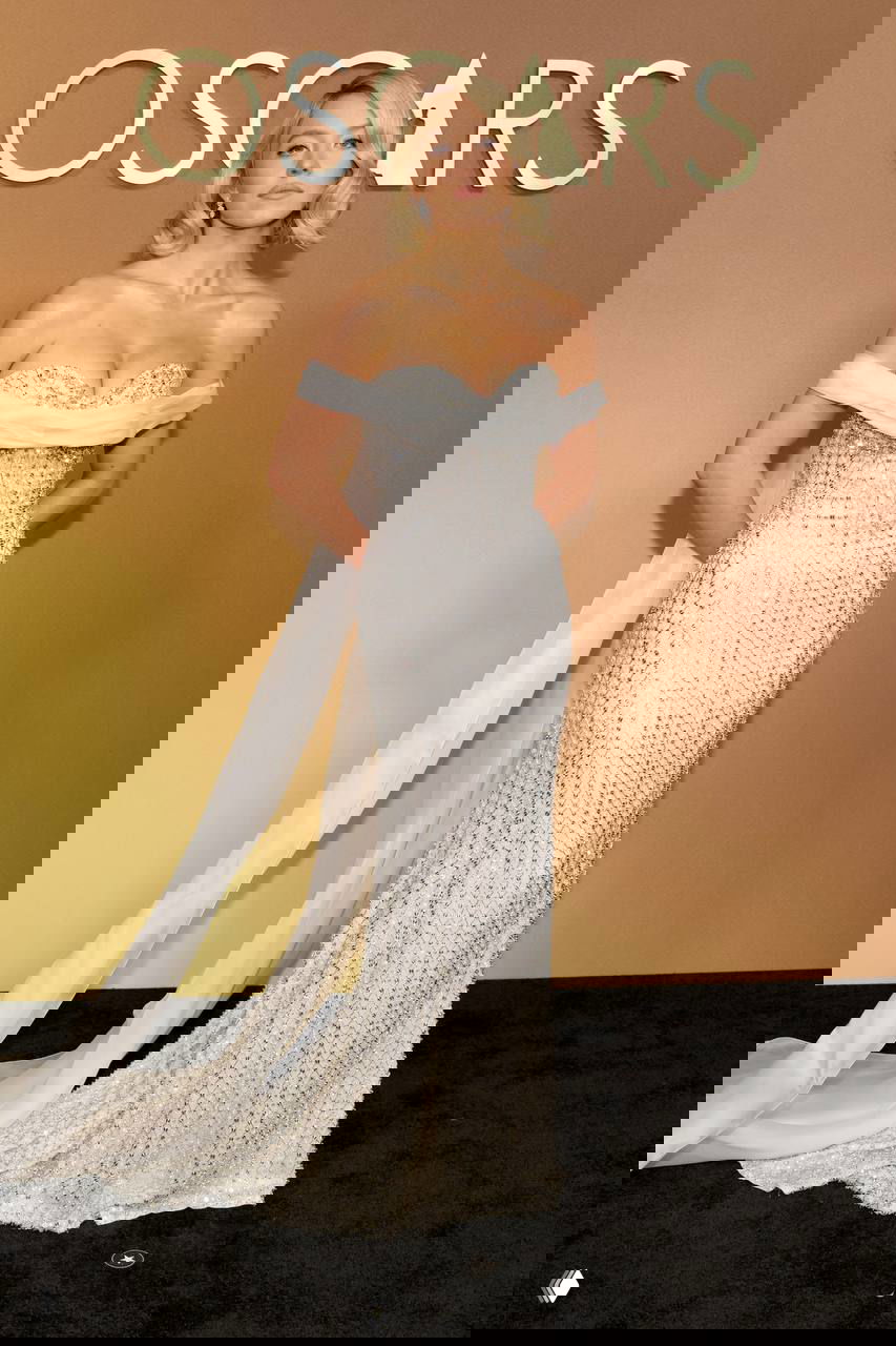 Женщина в серебристом облегающем платье с драпировкой и шлейфом на красной дорожке Governors Awards, портрет в полный рост на фоне бэкграунда, фотография с Governors Awards в Лос-Анджелесе.