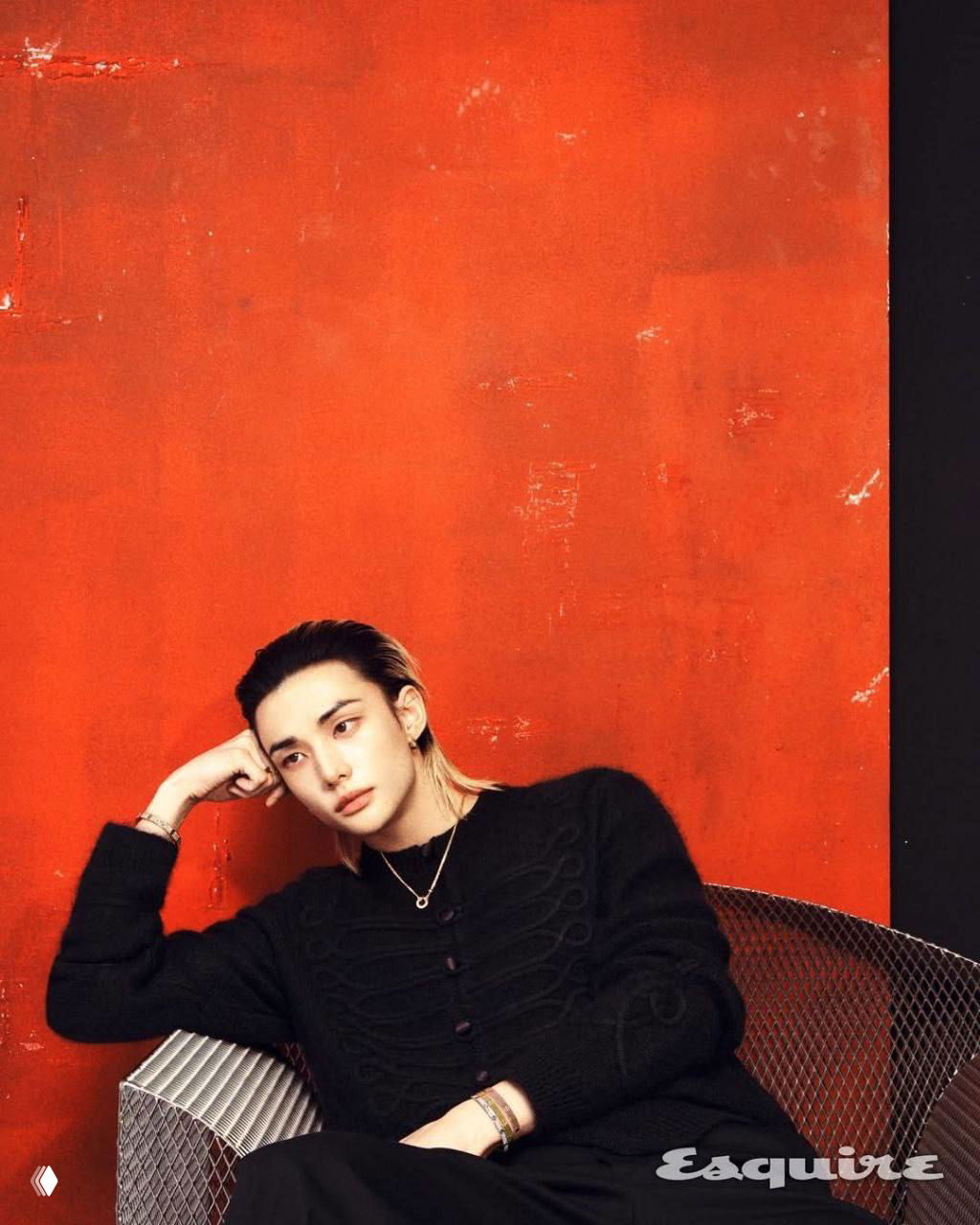 Фотография сидящего молодого айдола на стуле на красном фоне, расслабленная поза и стильный образ в рамках модной фотосессии для журнала.