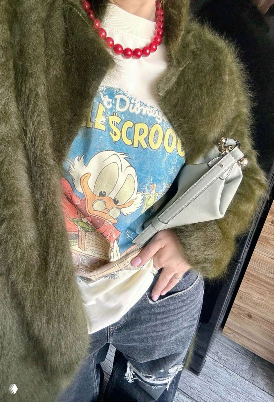 Фрагмент образа: зелёная пушистая шубка, винтажная футболка с мультгероем, сумка и детали повседневного стиля в отражении зеркала.