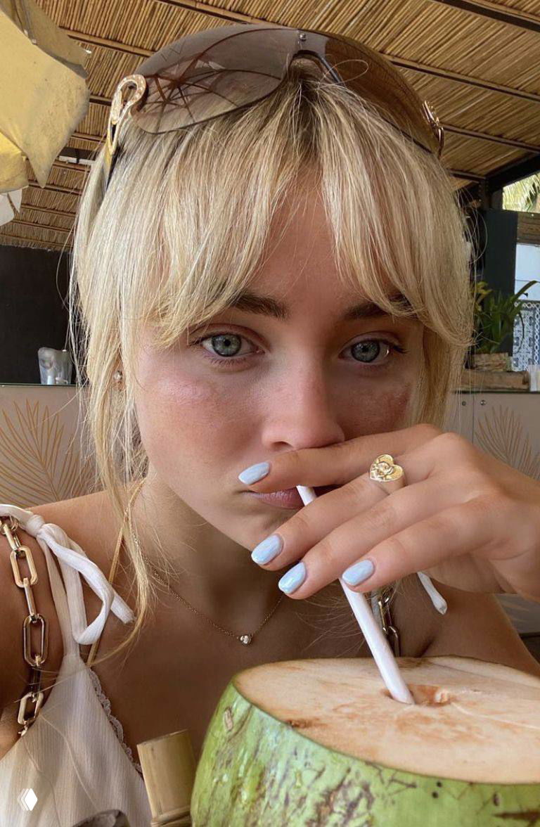 Крупный план уличного/кафе‑кадра: девушка с пастельным голубым маникюром пьет напиток из кокоса, естественный летний образ.