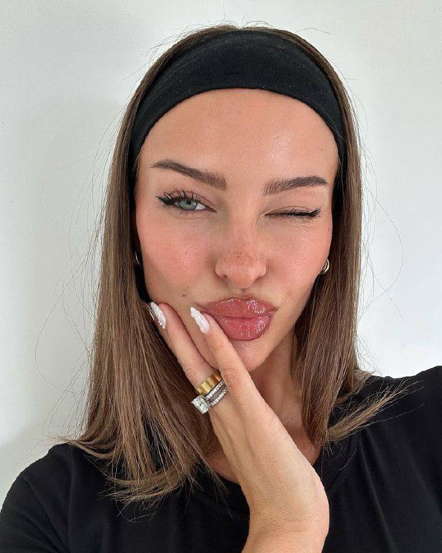 Крупный план лица женщины с глянцевой помадой и естественной кожей, лёгкий лавандовый румянец и аккуратные ресницы