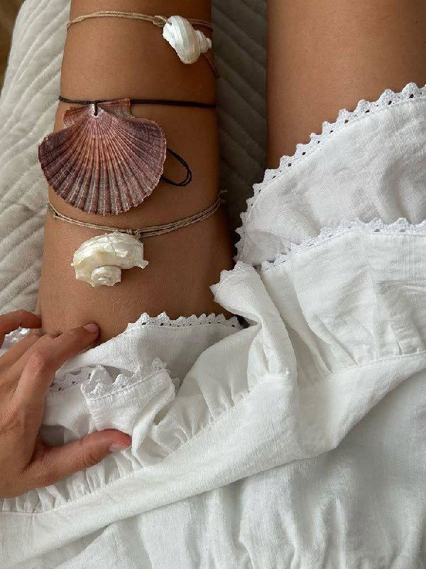 Ноги и руки с украшениями из ракушек на белой лёгкой ткани — эстетика пляжного стиля и натуральных пастельных тонов
