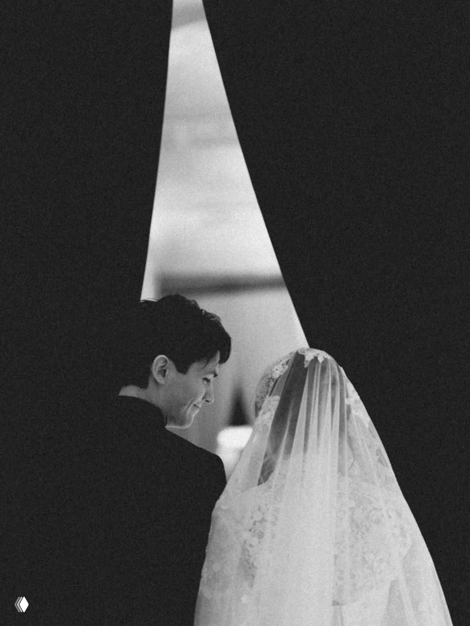 Чёрно‑белый портрет жениха и невесты: улыбающийся мужчина и вуаль невесты в интимной композиции, тихий эмоциональный момент.