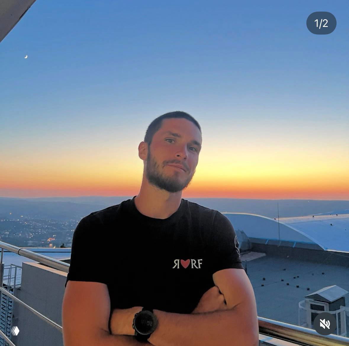 Спортсмен в футболке на балконе на фоне заходящего солнца: расслабленная поза, тёплые тона заката и панорама за спиной.