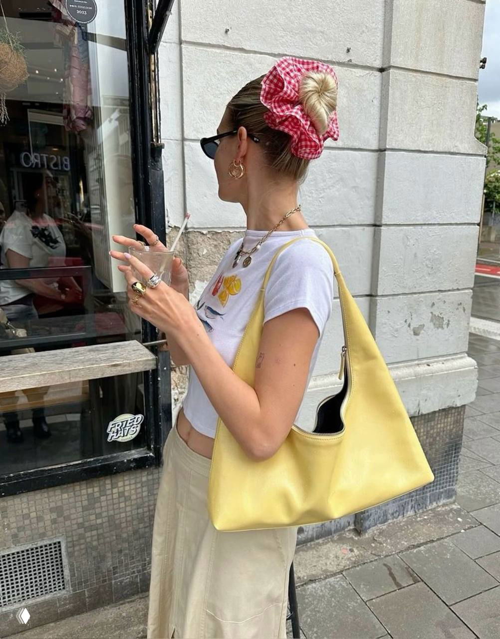 Девушка с пучком и красно-белой клетчатой резинкой у городского фасада: сочетание летнего стиля и яркого аксессуара в повседневном луке.