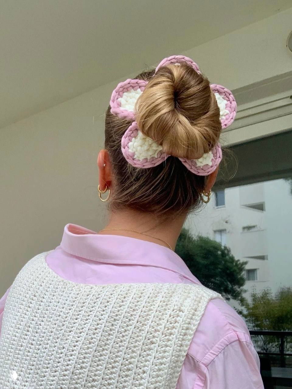 Пучок с вязаной розово-белой резинкой в форме цветка: мягкая текстура, нежные тона и акцент на аксессуаре на фоне жилого дома.