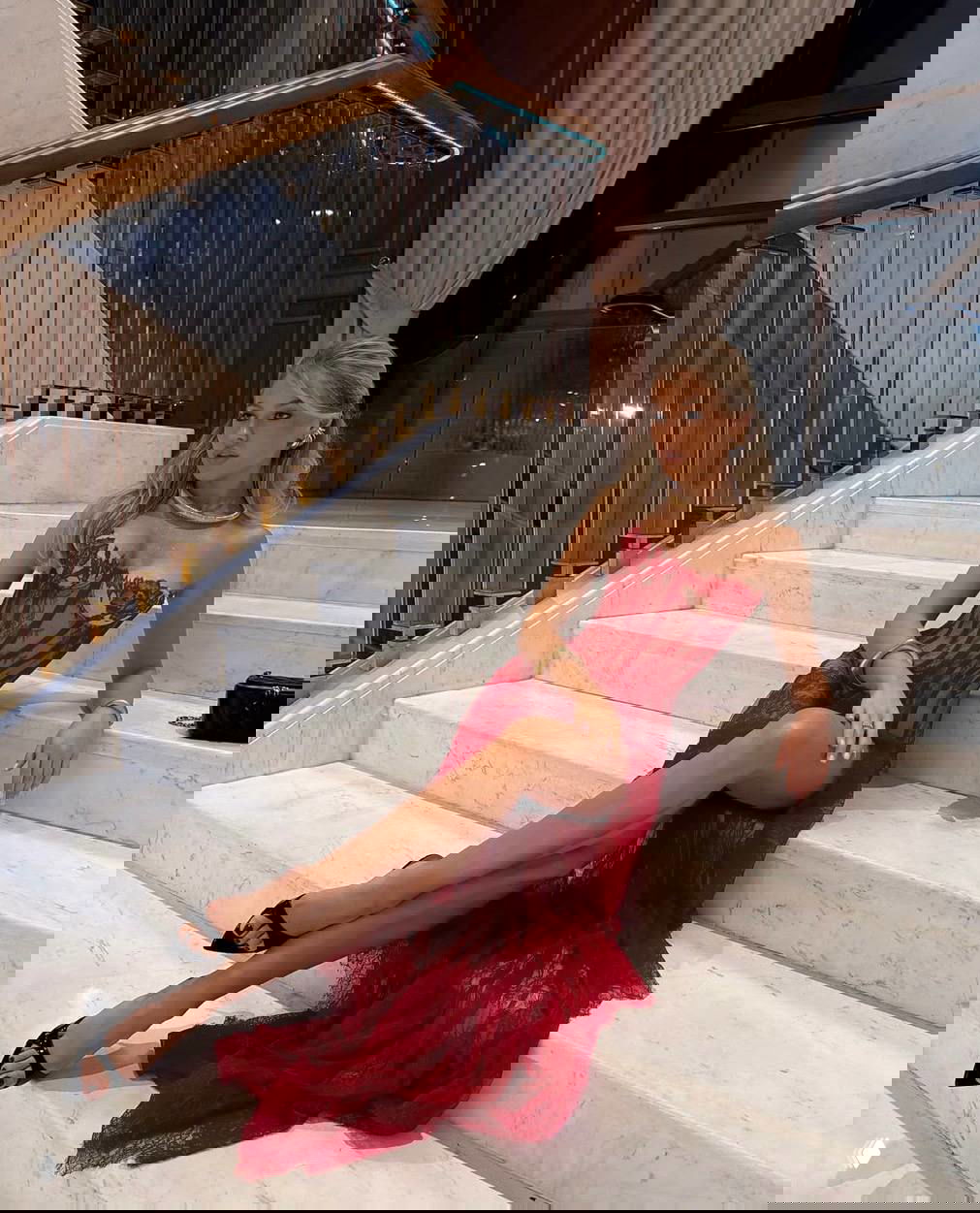 Катя в красном кружевном платье, сидящая на ступеньках — образ с акцентом на чёрные мюли и длинный шлейф платья в торжественной обстановке.