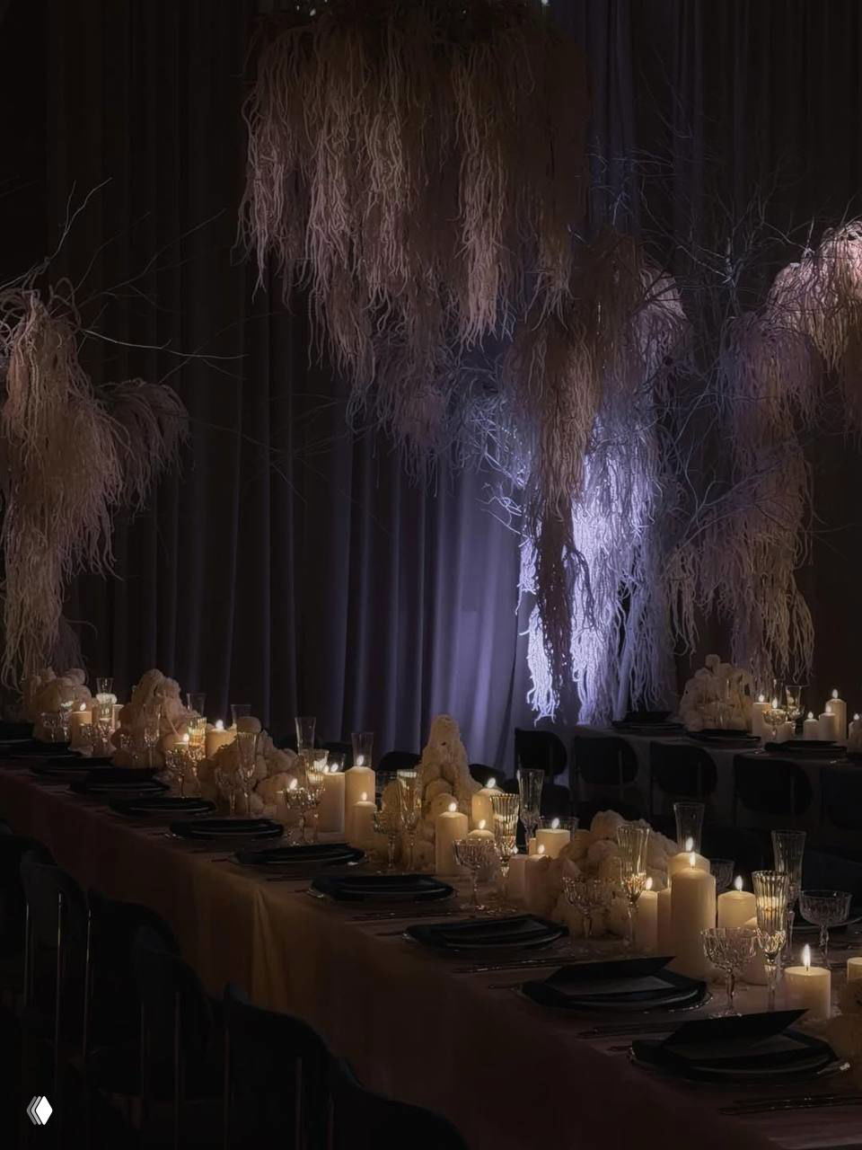 Оформление банкета: длинный стол при свечах и декоративные подвесные ветви, тёплая интимная сервировка в затемнённом зале для праздника.